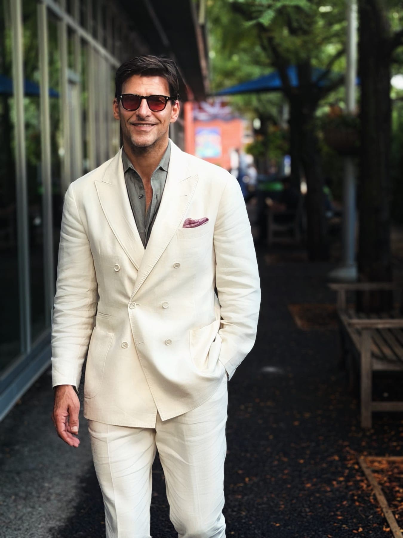 Person in a cream double-breasted suit on a leafy street