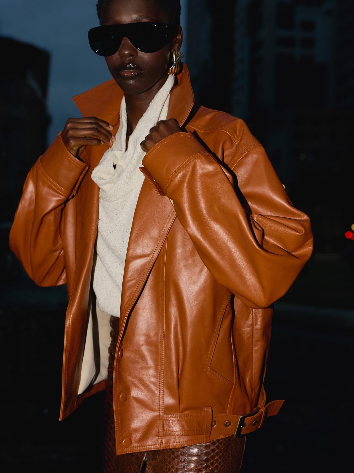 Person in a tan leather jacket and sunglasses at night